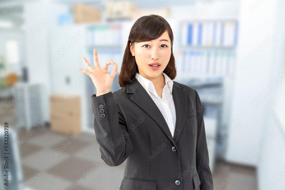 オフィスでOKサインをするカメラ目線のスーツを着た若い女性