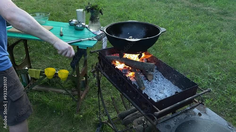 A handsome white man prepares a delicious meal in a cauldron over an open flame on a backyard grill. Outdoor cooking, barbecue tradition, backyard leisure, culinary skills with relaxation. BBQ concept