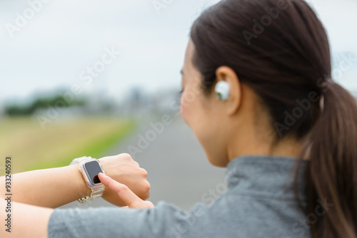 スマートウォッチを見てランニングをする女性