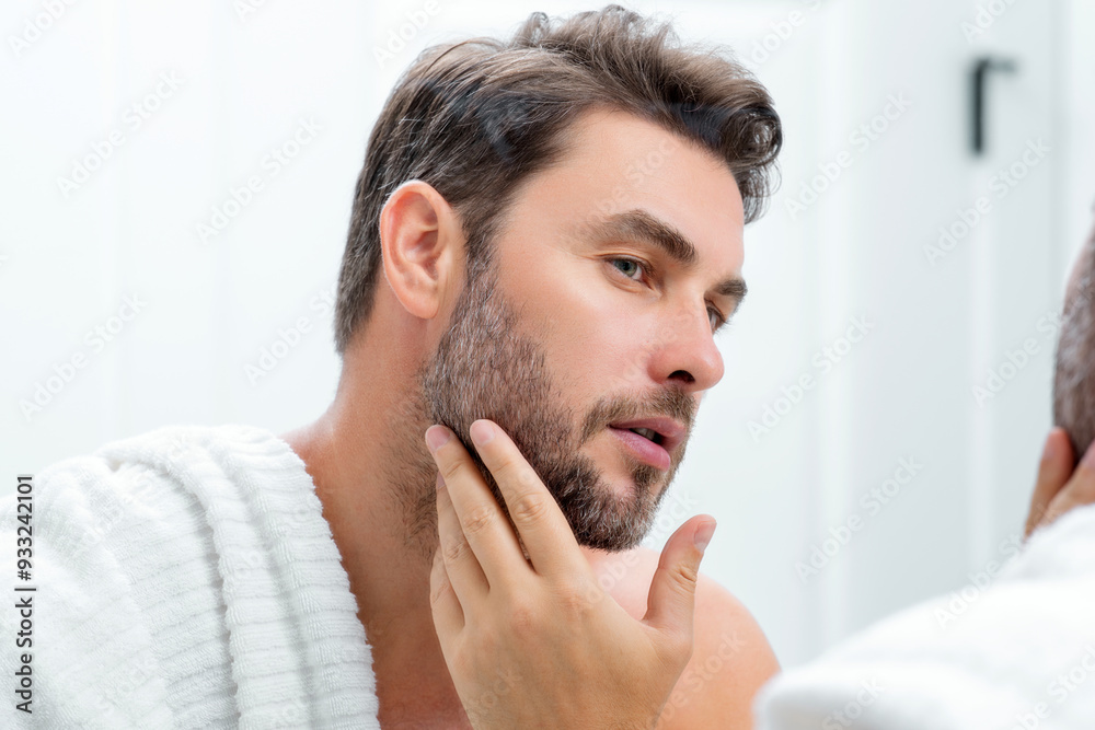 Obraz premium Millennial hispanic man looking in mirror, facial skin and stubble. Male beauty care product. Skincare, home spa. Beauty portrait of a beautiful man. Spa model, moisturizing nourishing creme.