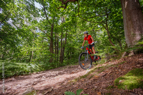 Happy teen boy ride red mountain bike through dense forest trail