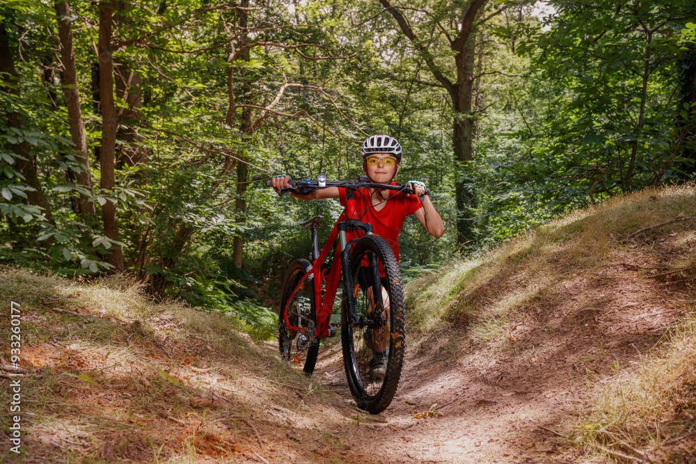 Biker kid in red shirt and helmet pushes bike up forest trail Biker kid in red shirt and helmet pushes bike up forest trail