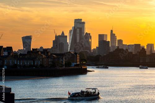 A boat sails peacefully on a river under the vibrant hues of a sunset with a city skyline in the background, symbolizing tranquility and urban lifestyle juxtaposed in London England photo