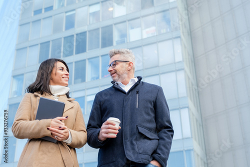 Two corporate professionals engage in a friendly discussion as they stroll outside their office in the financial district