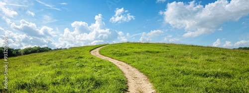  A winding path ascending a grassy hill against a backdrop of a blue sky, dotted with white clouds, and featuring a lush, green foreground