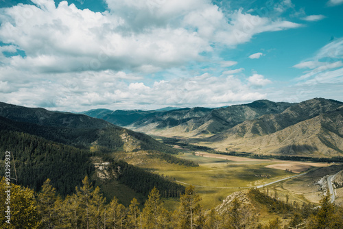 A breathtaking view of green valleys and rugged mountains under a bright blue sky creates a stunning landscape in the Altai Mountains