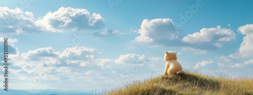  A  bear atop a green hill's peak, beneath a blue sky adorned with cottony white clouds
