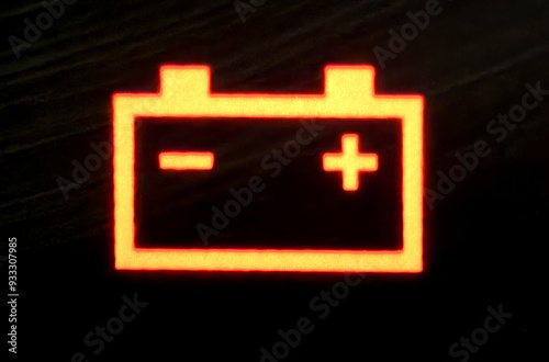 An extremely close-up picture of a battery light signal glowing on the dashboard.
