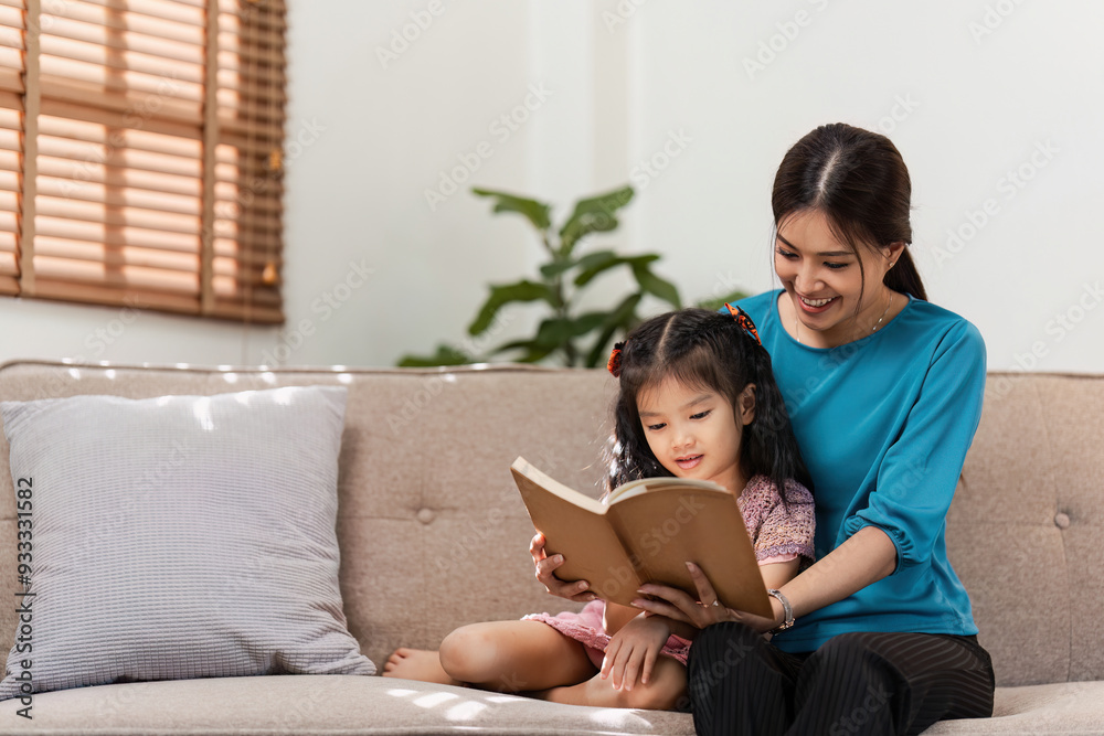 Mother and Daughter Reading a Book Together on a Cozy Sofa in a Bright Living Room Mother and Daughter Reading a Book Together on a Cozy Sofa in a Bright Living Room