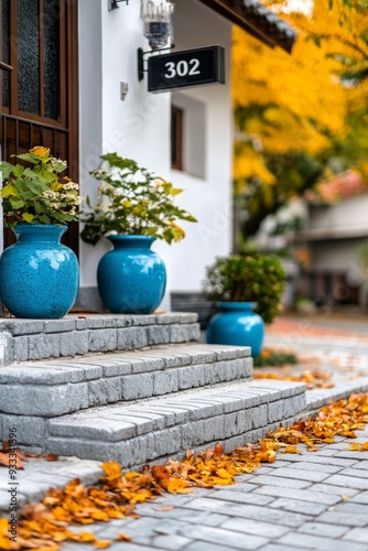 Autumn leaves adorn steps leading to a vibrant blue door with potted plants