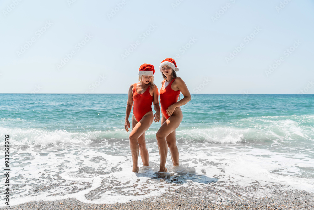 Women Santa hats ocean play. Seaside, beach daytime, enjoying beach fun. Two women in red swimsuits and Santa hats are enjoying themselves in the ocean waves and raising their hands up. Women Santa hats ocean play. Seaside, beach daytime, enjoying beach fun. Two women in red swimsuits and Santa hats are enjoying themselves in the ocean waves and raising their hands up.