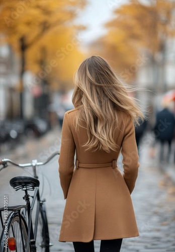 Woman walking in a stylish coat down a cobbled street with a bicycle beside her