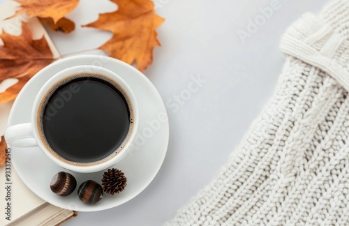 Warm coffee cup with latte art and autumn leaves beside a cozy sweater on a book
