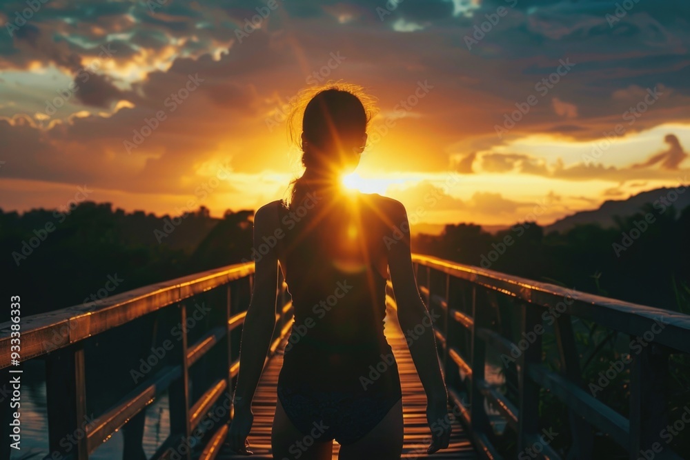 Fototapeta premium A woman stands on a bridge as the sun sets behind her, casting a warm glow