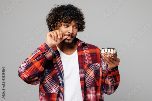 Cuadro en lienzo Young sad tempted dissatisfied Indian man he wears red shirt casual clothes hold in hand look at piece of cake lick finger isolated on plain grey color background studio portrait