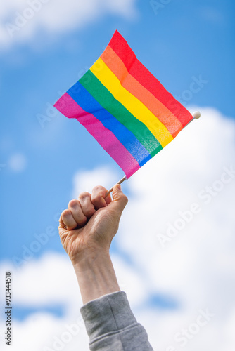 Hand holds up rainbow pride flag against the sky
