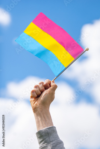 Hand holds up pansexual pride flag against sky