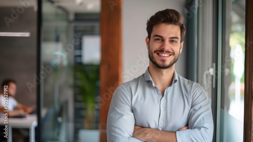 Smiling handsome businessman with crossed arms in modern office, young man exuding confidence, business success concept.