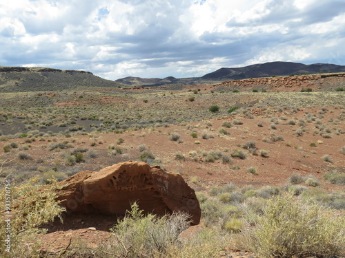 Red Rock in Foreground of Desert Scrub Brush Landscape in Front of Hills under Sunlit Gray and White Cloudy Sky photo