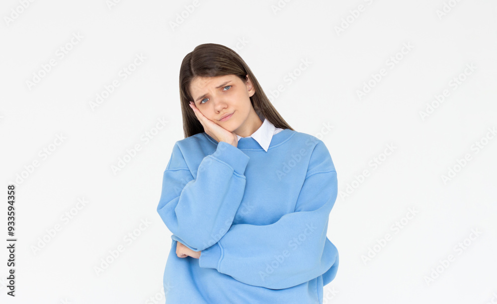 Cute woman standing in blue sweatshirt, holding palm on cheek and leaning face on it, being bored and tired of uninteresting talks, feeling indifferent to what happening over white wall Cute woman standing in blue sweatshirt, holding palm on cheek and leaning face on it, being bored and tired of uninteresting talks, feeling indifferent to what happening over white wall