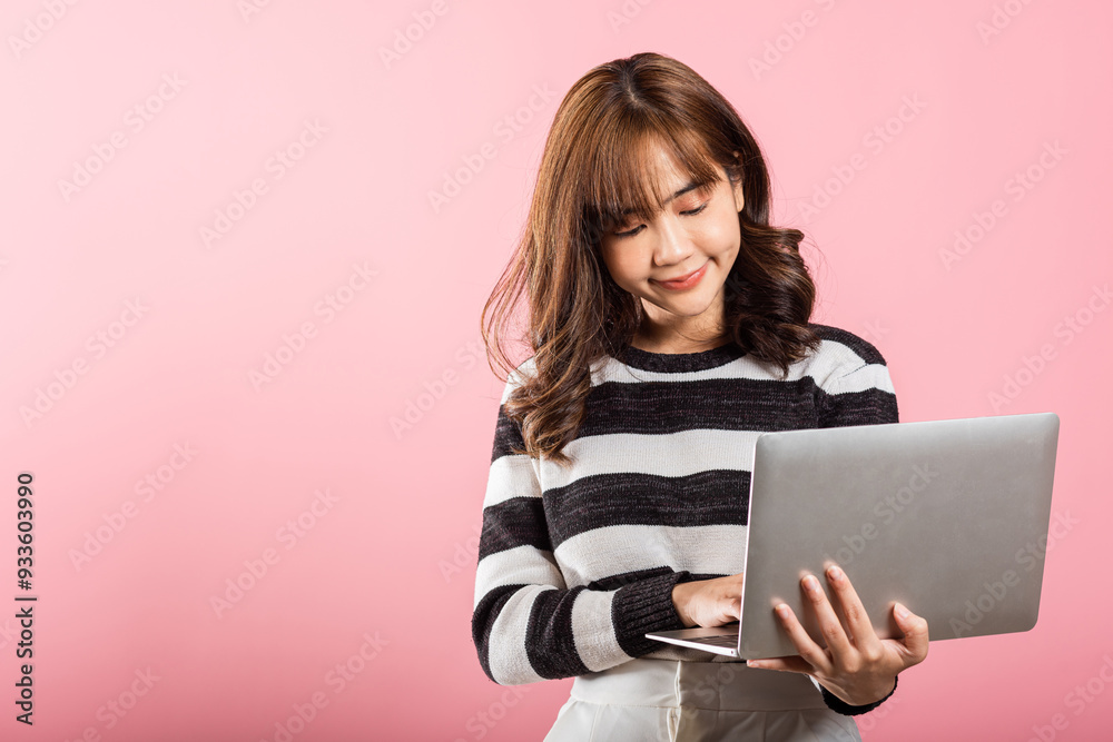 Portrait of happy Asian beautiful young woman confident smiling face holding using laptop computer looking to camera, studio shot isolated on pink background with copy space, notebook computer