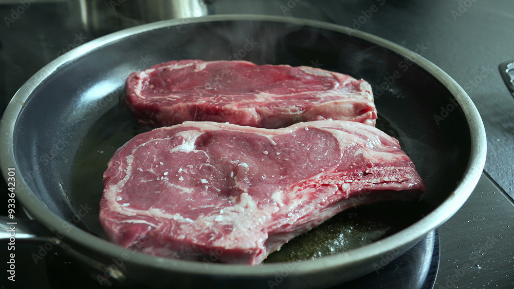 Raw steaks sizzling in a hot pan, lightly salted, beginning to cook, close-up view of fresh beef, home cooking process, preparing a delicious meal, culinary detail, kitchen scene Raw steaks sizzling in a hot pan, lightly salted, beginning to cook, close-up view of fresh beef, home cooking process, preparing a delicious meal, culinary detail, kitchen scene