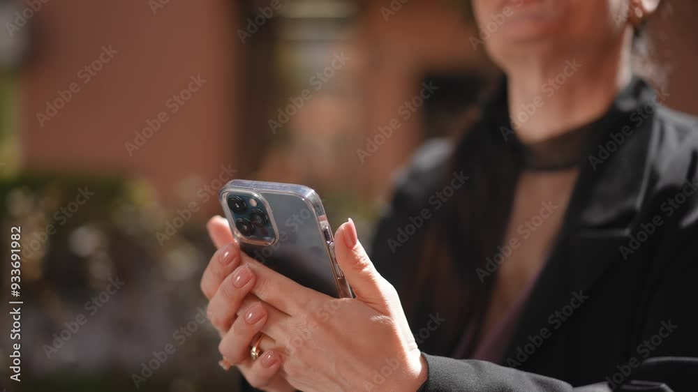 Close-up. A woman wearing glasses holds a mobile phone in her hand and taps on the screen, while standing outdoors on a sunny spring day Close-up. A woman wearing glasses holds a mobile phone in her hand and taps on the screen, while standing outdoors on a sunny spring day