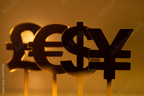 Close-up of four different currency symbols: the U.S. dollar, the British pound, the Euro,and the Japanese yen, on sticks in front of a gold background photo