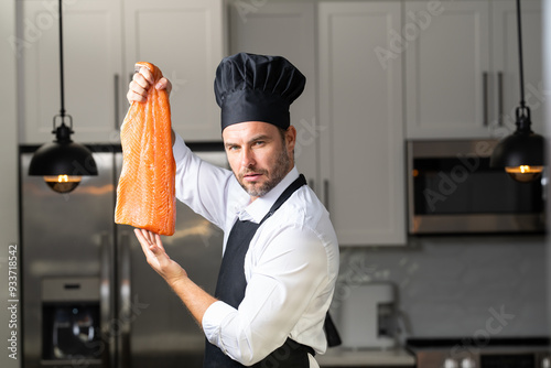 A chef is holding a piece of salmon in his hand and wearing a black hat. High quality photoA chef is holding a piece of salmon in his hand and wearing a black hat. Concept expertise in the kitchen photo