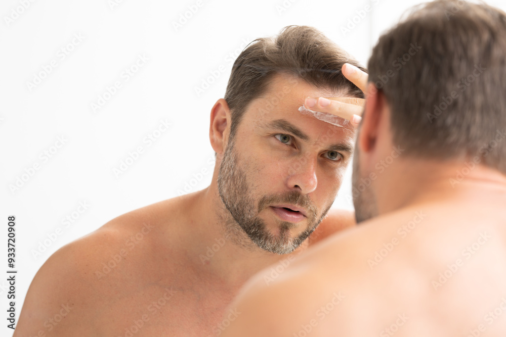 A man is applying lotion to his face in front of a mirror. Concept of self-care and personal grooming A man is applying lotion to his face in front of a mirror. Concept of self-care and personal grooming