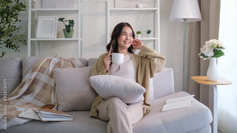 Carefree young woman sitting comfortably on sofa, holding a mug and enjoying quiet moment at home. Carefree young woman sitting comfortably on sofa, holding a mug and enjoying quiet moment at home.