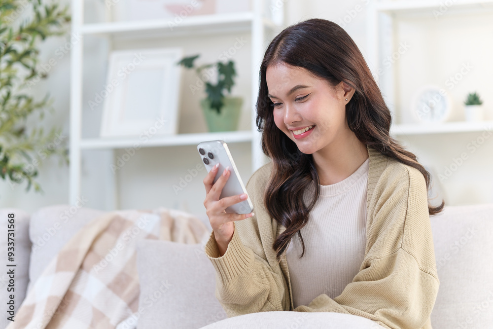 Beautiful young woman sitting comfortably on a couch in living room, looks at her smartphone. Beautiful young woman sitting comfortably on a couch in living room, looks at her smartphone.