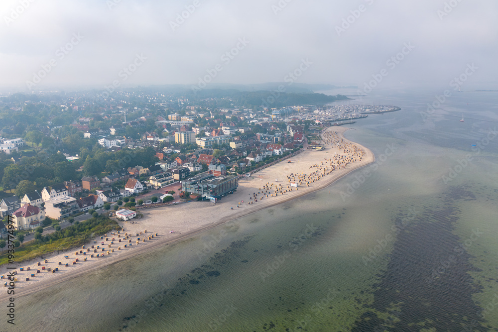 Fototapeta premium Aerial drone image of traditional numbered wicker, reed beach hut, or chair on the sand beach at the coastline of Laboe, the Baltic Sea in summer Germany with wooden walkway or path on cloudy day