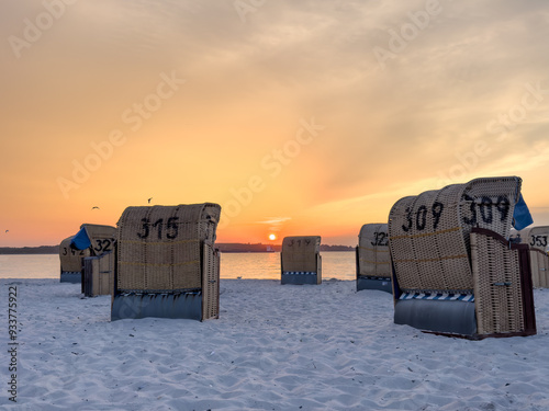Fototapeta Naklejka Na Ścianę i Meble -  Traditional numbered wicker, reed beach hut, or chair on the sand beach at the coastline of the Baltic Sea in summer Germany at sunset, sunrise