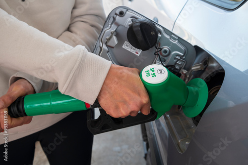 Woman's hand filling car with SP95 E10 petrol, green nozzle in use at a French petrol station
