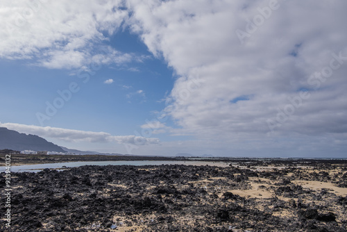 White sand beach with black rocks of volcanic origin. Mountains in the background and sky with big white clouds. Caletón Blanco, Lanzarote, Canary Islands, Spain