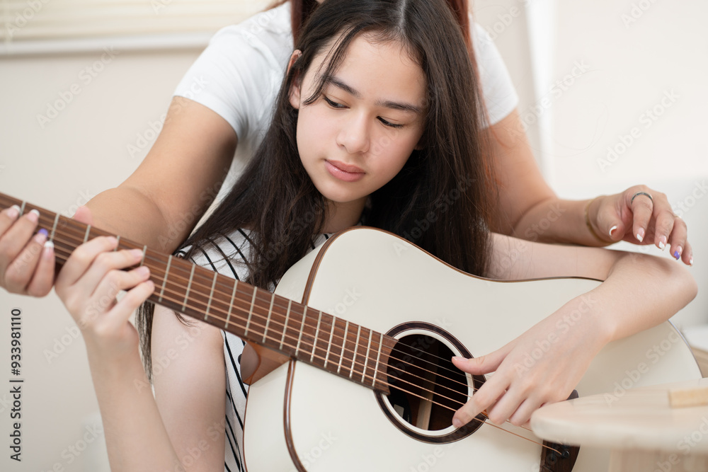 Fototapeta premium Teenager woman playing guitar with mother teaching at home 