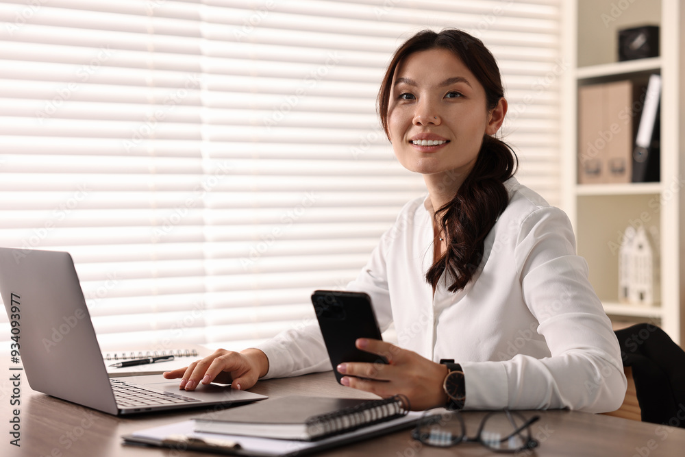 Smiling businesswoman with smartphone at table in office Smiling businesswoman with smartphone at table in office