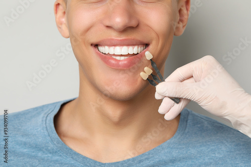 Doctor checking young man's teeth color on gray background, closeup. Dental veneers