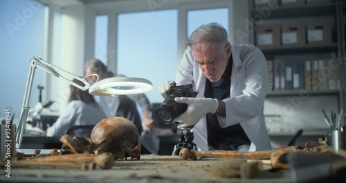 Fotografía Senior archaeologist takes photo of fossil remains of prehistoric human skull and bones with camera in modern archaeological lab