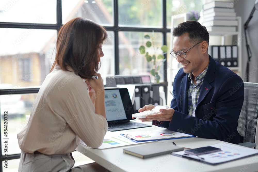 Asian businessman is showing a calculator to his female colleague while working together in the office Asian businessman is showing a calculator to his female colleague while working together in the office