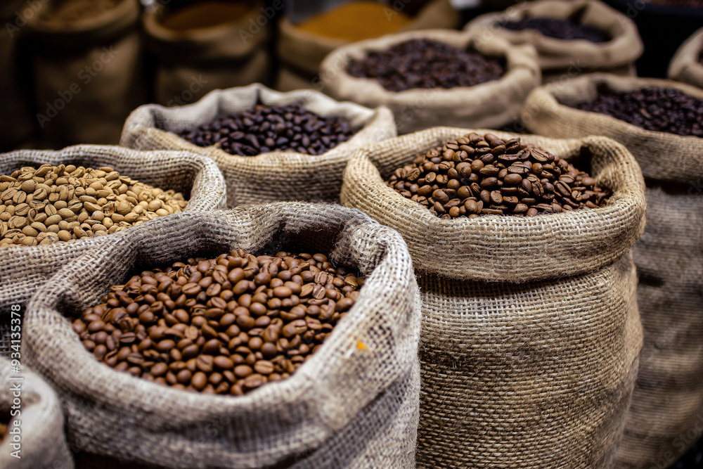 Selection of coffee beans in burlap sacks, with various roast levels and origins, displayed in a market setting.