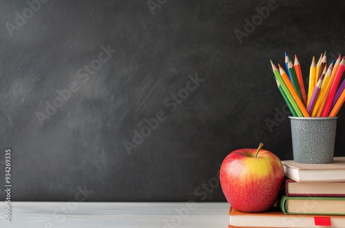 Colorful pencils in a black pot beside stacked books and an apple on a desk