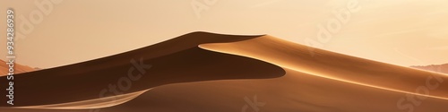 Minimalist image of a sand dune at sunset showcasing the smooth golden contours of the dune contrasted with a softly lit sky