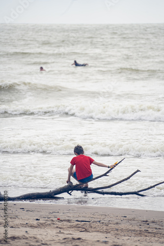 Young child on branches on the beach by the ocean