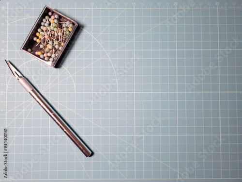 Isolated exacto knife and pins on blue cutting matt background