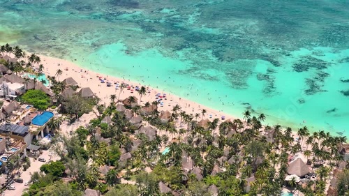 Aerial drone view of turquoise blue Caribbean Sea with beach cabins surrounded by green tropical palm trees on a sunny day in Mexico 