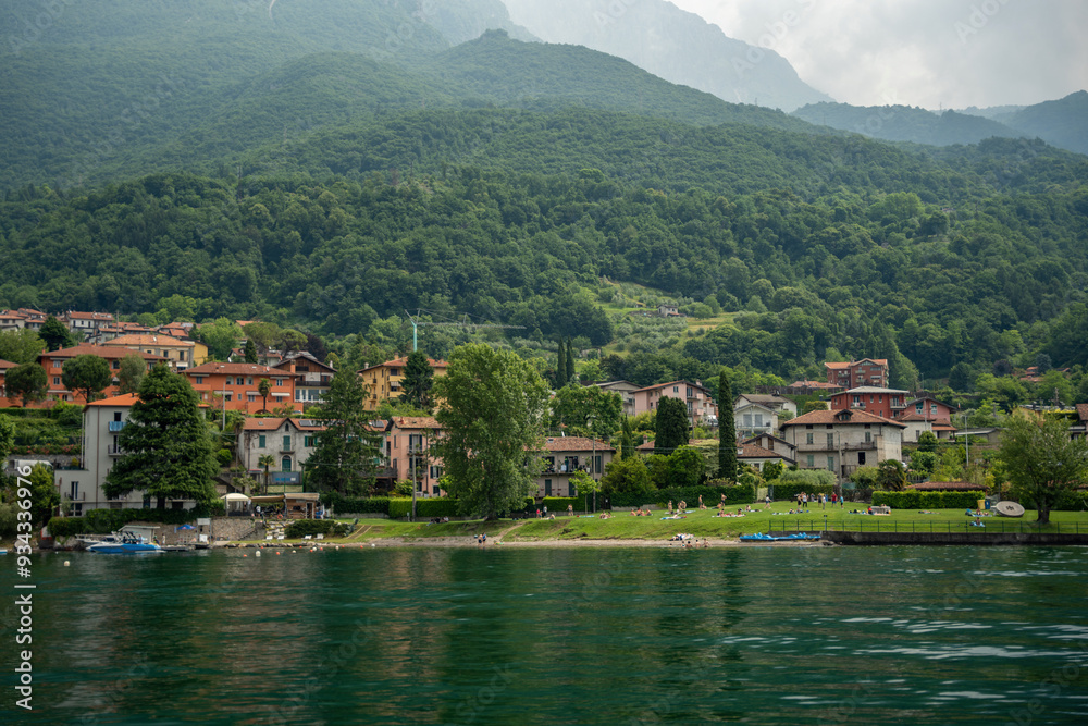 Fototapeta premium Mandello del Lario, Italy - June 08, 2024: Como lake mountains. Small village on the middle ground.