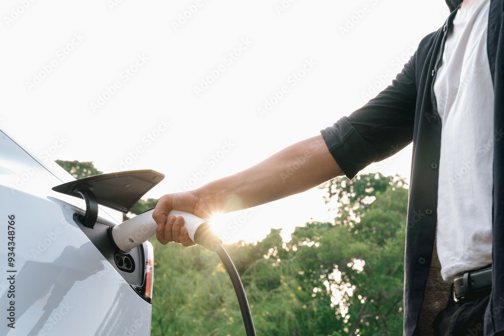 Φωτογραφία Man recharging battery for electric car during road trip travel EV car in natural forest or national park with sunrise lighting