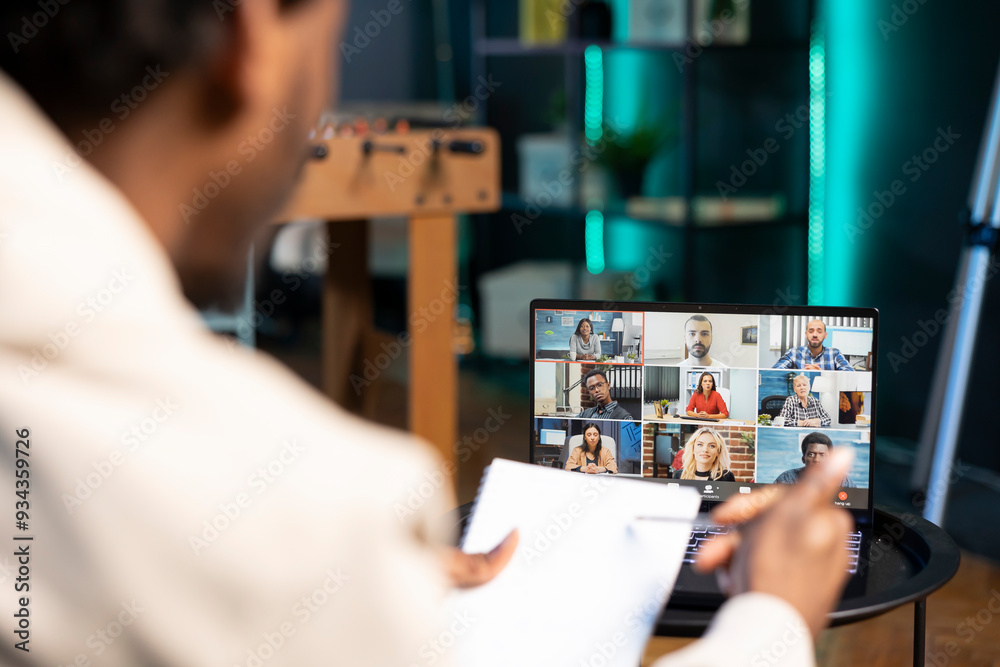 Remote employee in video conference meeting chatting with multi ethnic international team while working from home. Self employed man in online video call with coworkers in apartment Remote employee in video conference meeting chatting with multi ethnic international team while working from home. Self employed man in online video call with coworkers in apartment